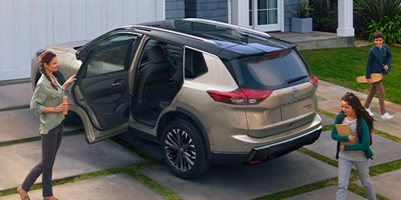 A family with a woman and two kids near a light beige 2025 Nissan Rogue SUV parked in a driveway.