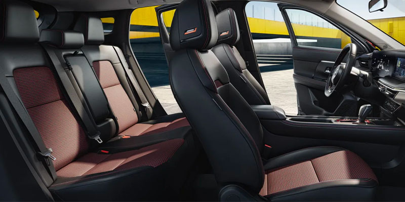 Interior of a 2025 Nissan Kicks crossover SUV showing black and red seats with seatbelts, sleek design and modern dashboard.